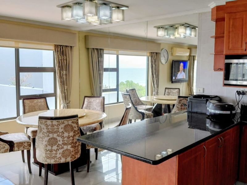 Open-plan kitchen and dining area featuring granite countertops, wooden cabinetry, and large windows with ocean views, creating a bright and functional living space.