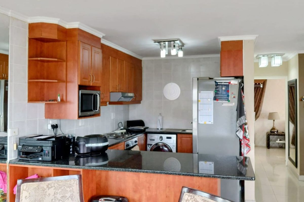 A functional kitchen featuring wooden cabinetry, granite countertops, a tiled backsplash, and integrated laundry facilities, offering a practical layout for daily use.