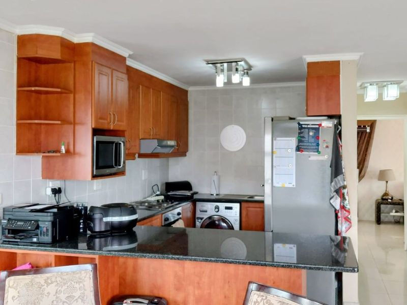 A functional kitchen featuring wooden cabinetry, granite countertops, a tiled backsplash, and integrated laundry facilities, offering a practical layout for daily use.