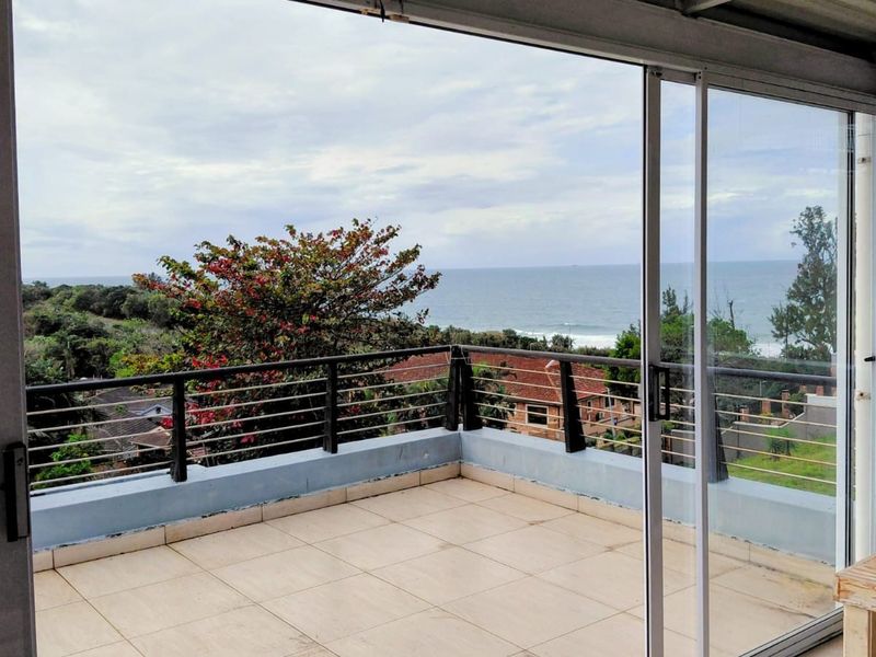 Spacious balcony featuring tiled flooring, metal railings, and expansive sliding glass doors with scenic ocean views.
