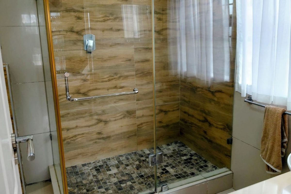 A modern bathroom featuring a walk-in shower with glass enclosure, wood-effect wall tiling, mosaic floor tiles, and a contemporary vessel sink.