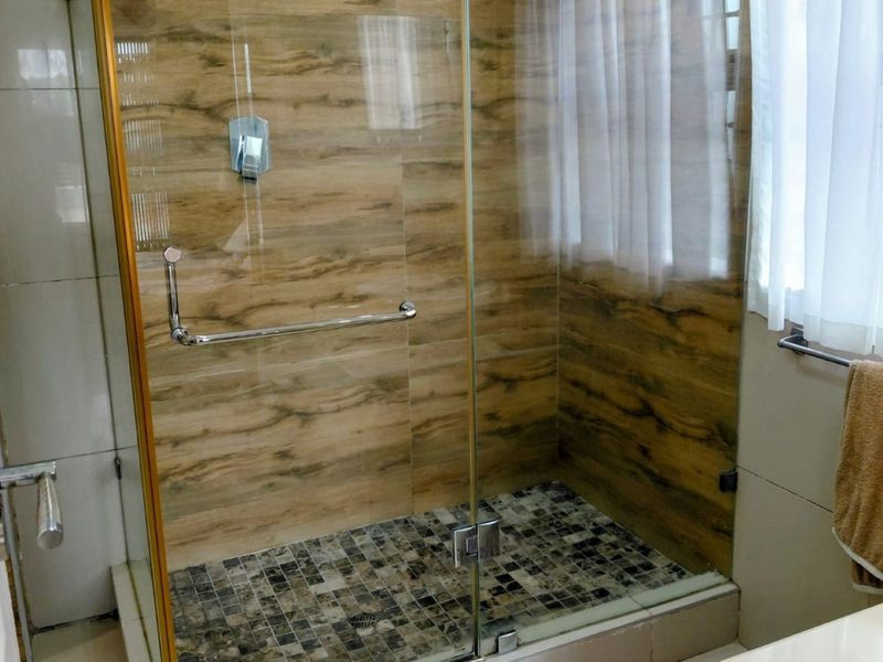 A modern bathroom featuring a walk-in shower with glass enclosure, wood-effect wall tiling, mosaic floor tiles, and a contemporary vessel sink.