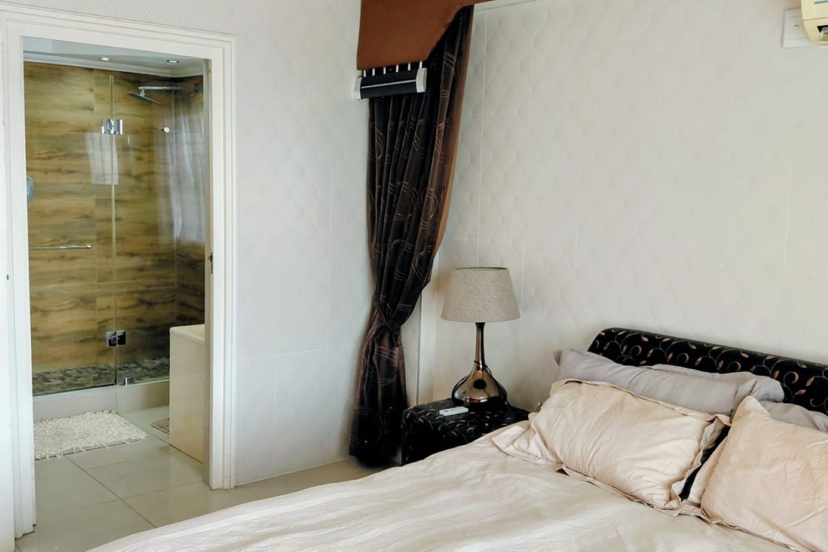 A bedroom featuring tiled flooring, a wall-mounted air conditioning unit, and direct access to an en-suite bathroom with a glass-enclosed shower.