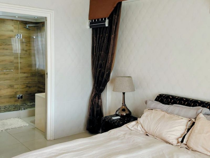 A bedroom featuring tiled flooring, a wall-mounted air conditioning unit, and direct access to an en-suite bathroom with a glass-enclosed shower.