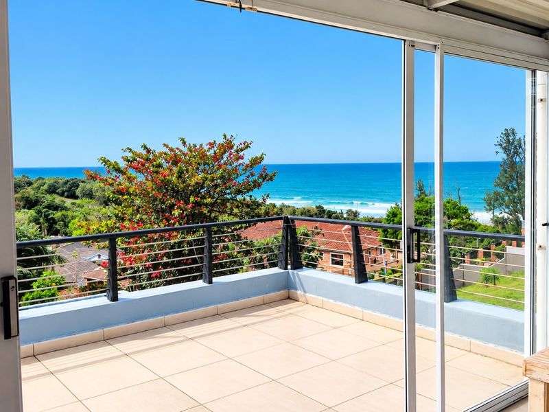 A spacious covered balcony featuring tiled flooring, a modern metal balustrade, and expansive sliding glass doors offering panoramic ocean views.