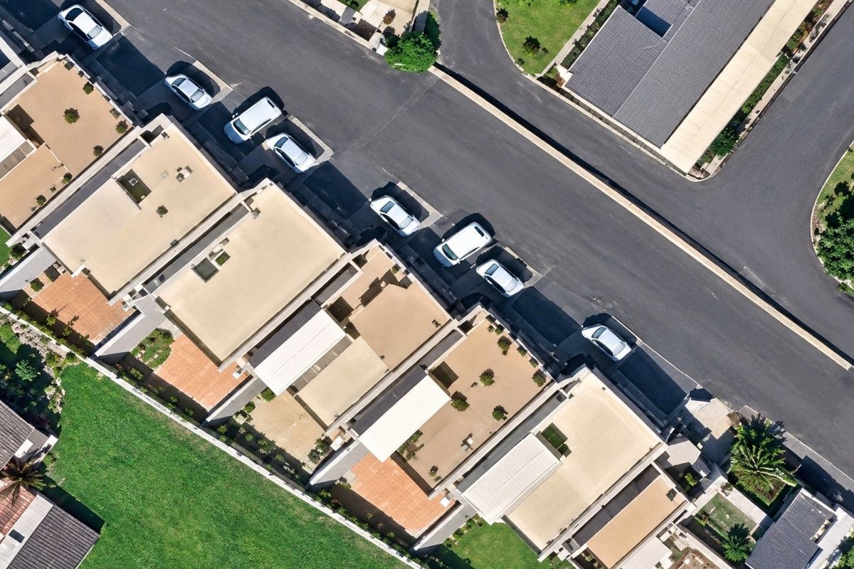 An aerial view of a residential apartment complex showing the building layout, flat roof structures, paved driveways, and surrounding landscaped garden areas.
