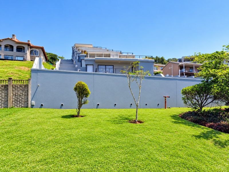 A view of the rear exterior of the apartment complex, featuring a well-maintained lawn, boundary wall, and tiered balconies.