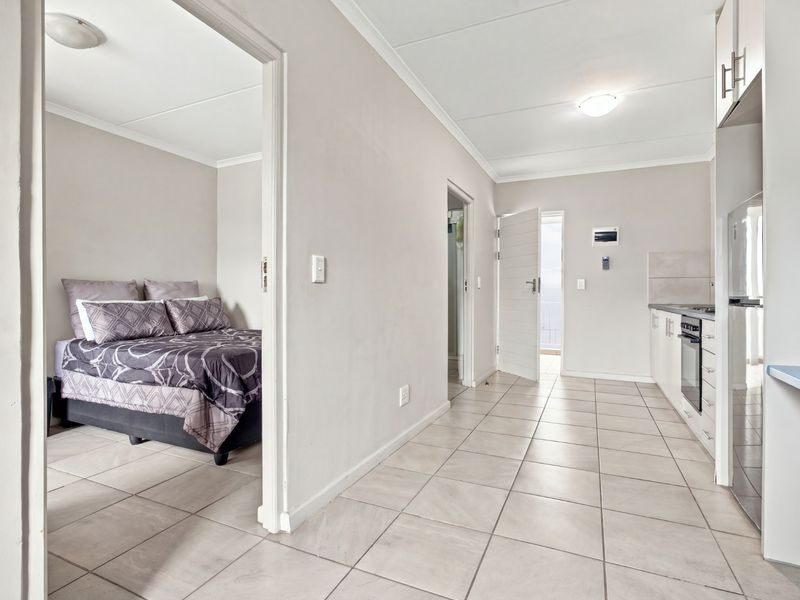 Open plan living area featuring tiled flooring, a functional kitchen with built-in cabinetry and appliances, and direct access to an adjoining bedroom.