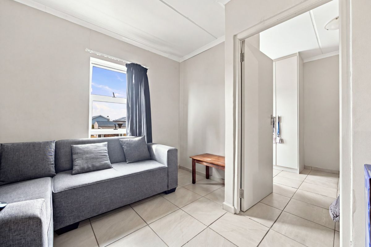 A bedroom featuring tiled flooring, built-in cupboards, and a window, with an adjacent walk-through area.