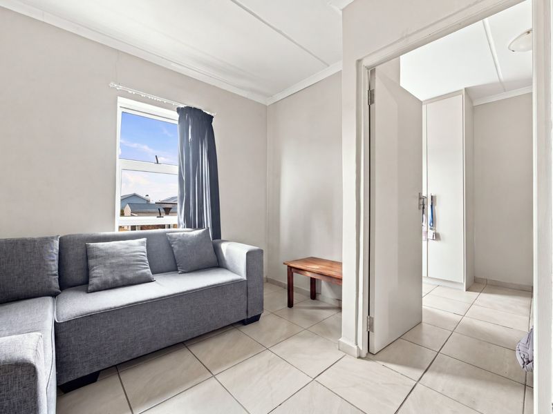 A bedroom featuring tiled flooring, built-in cupboards, and a window, with an adjacent walk-through area.