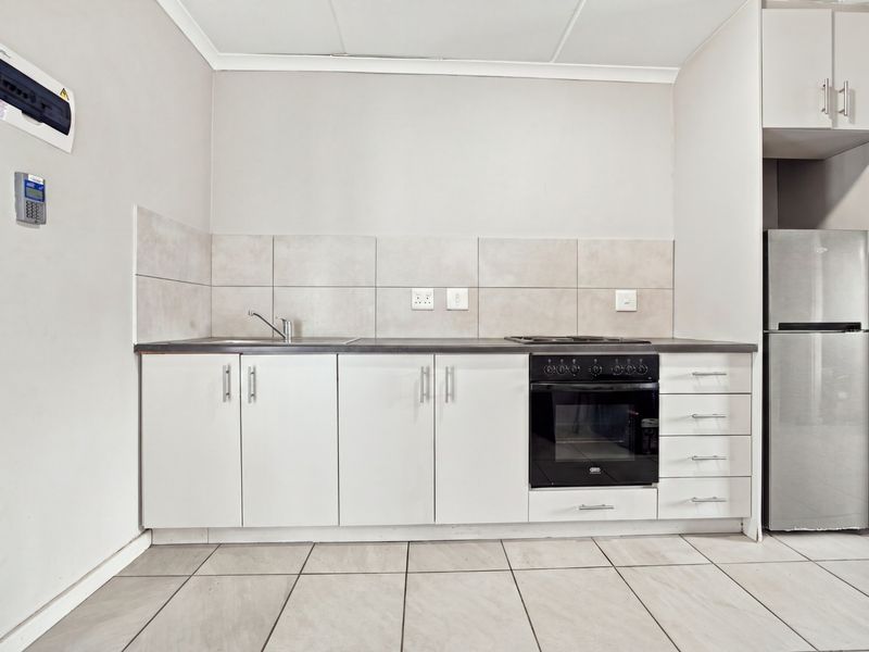 A clean, functional kitchen featuring white cabinetry, a built-in oven with hob, tiled splashbacks, and neutral floor tiles in an open-plan layout.