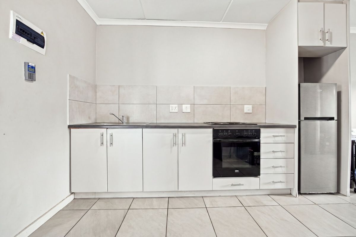 A clean, functional kitchen featuring white cabinetry, a built-in oven with hob, tiled splashbacks, and neutral floor tiles in an open-plan layout.