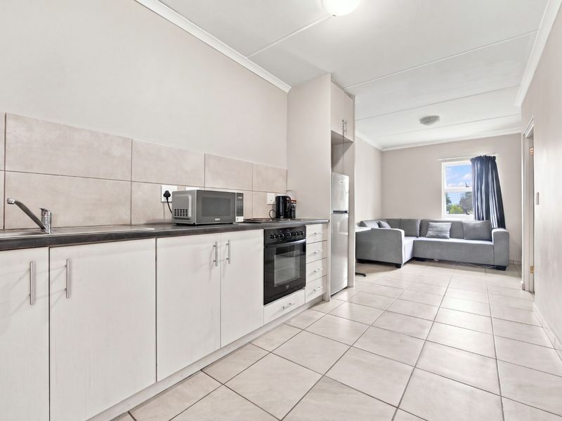 Open-plan kitchen and living area featuring neutral cabinetry, tiled flooring, and a functional layout with integrated oven and sink.