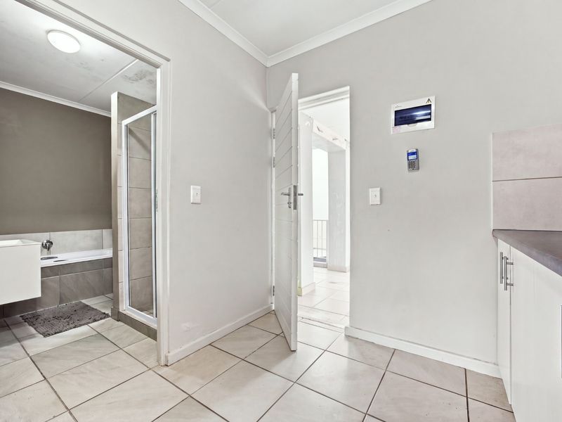 A tiled hallway area featuring an intercom system, security alarm panel, and access to an adjacent bathroom and balcony.