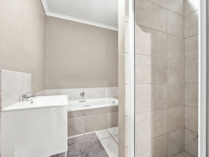 A clean, modern bathroom featuring a built-in bathtub, vanity basin, and a separate tiled shower enclosure with neutral finishes.