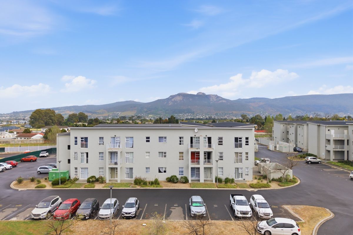 Aerial view of a multi-story apartment complex featuring dedicated parking bays, landscaped garden areas, and scenic mountain views in the background.