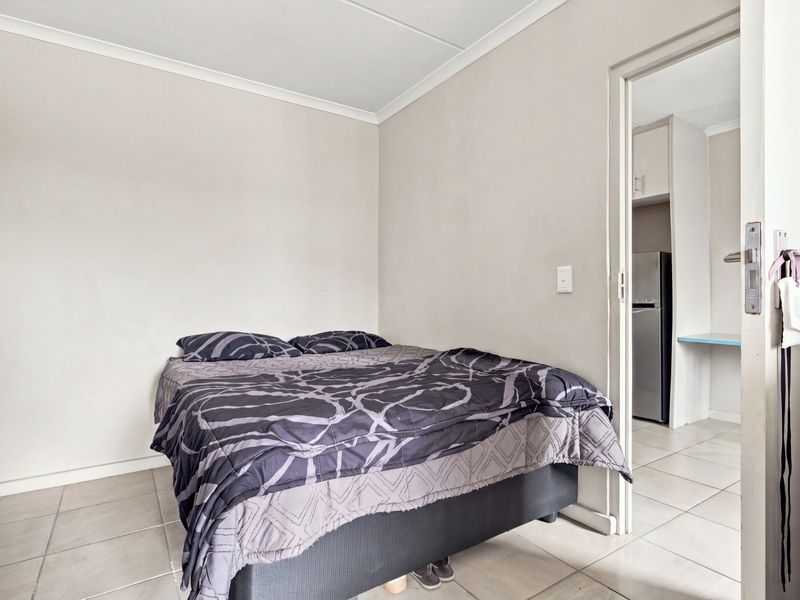 A bedroom featuring neutral wall finishes and tiled flooring, with an adjacent view into a kitchen area.
