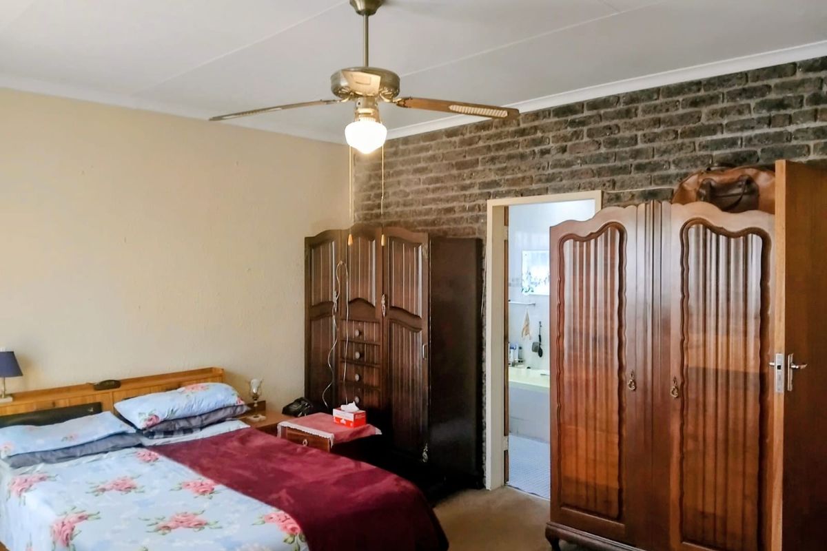 A bedroom featuring an exposed brick feature wall, ceiling fan, and direct access to an adjoining bathroom.
