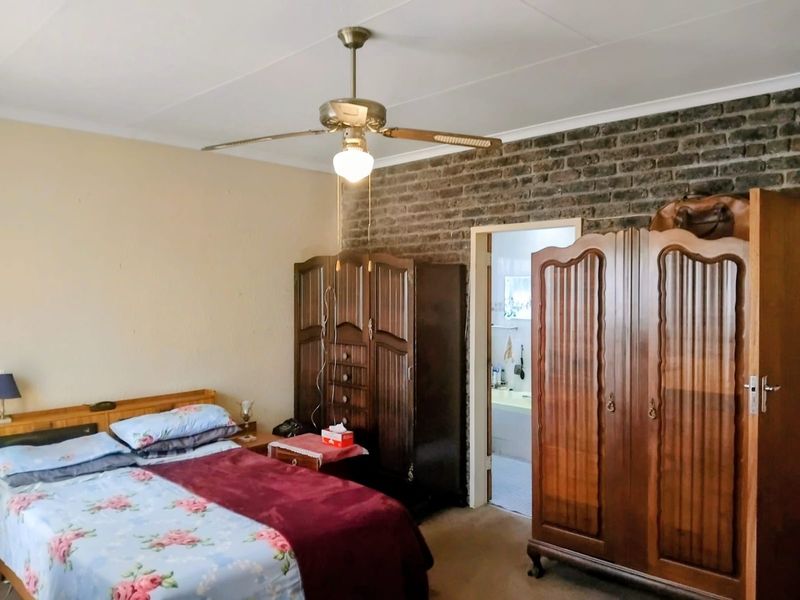 A bedroom featuring an exposed brick feature wall, ceiling fan, and direct access to an adjoining bathroom.