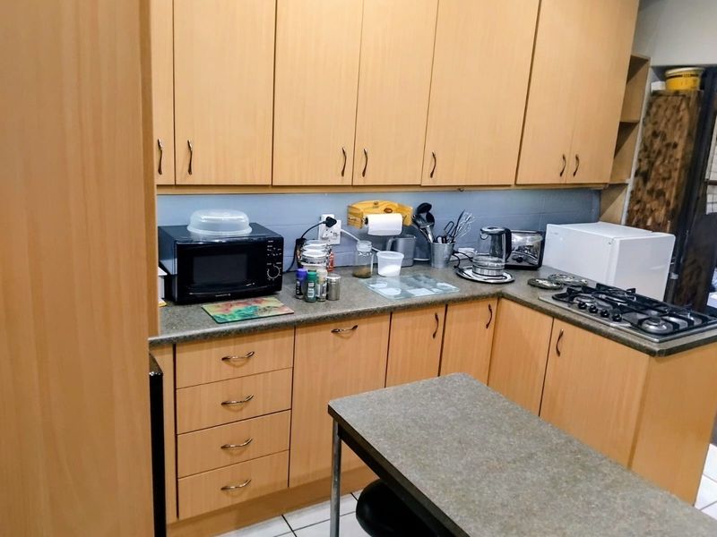 A functional kitchen featuring light wood-tone cabinetry, laminate countertops, and a built-in gas hob with tiled flooring.