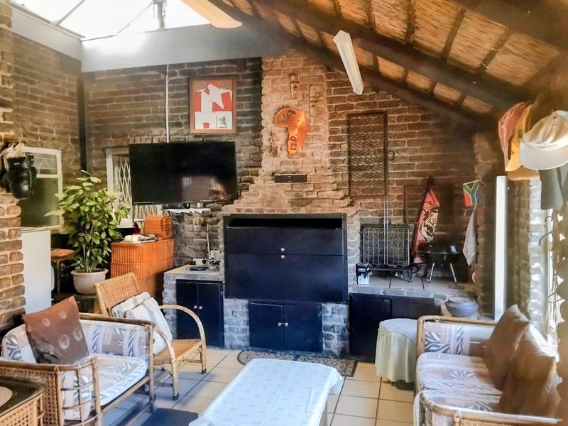 Covered patio area featuring exposed brick walls, a built-in braai, tiled flooring, and a thatched roof with a skylight.