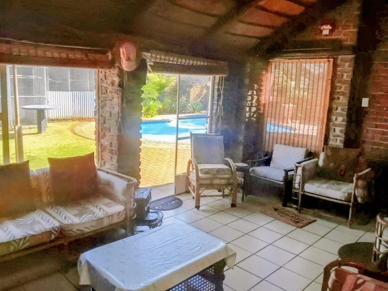 Covered patio area featuring exposed brick walls, tiled flooring, and timber beam ceiling, with direct access to the outdoor pool area.