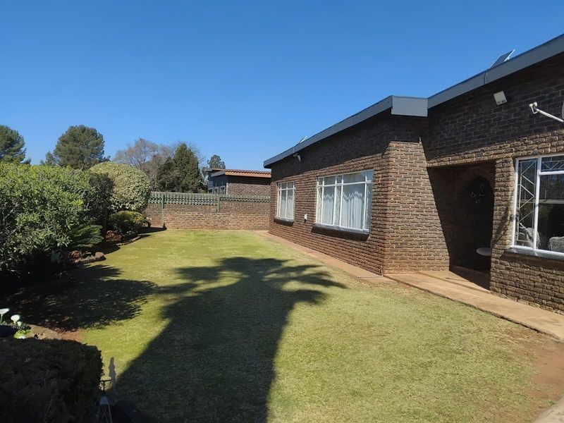 A well-maintained rear garden featuring a neat lawn, face brick exterior walls, and secure window treatments.