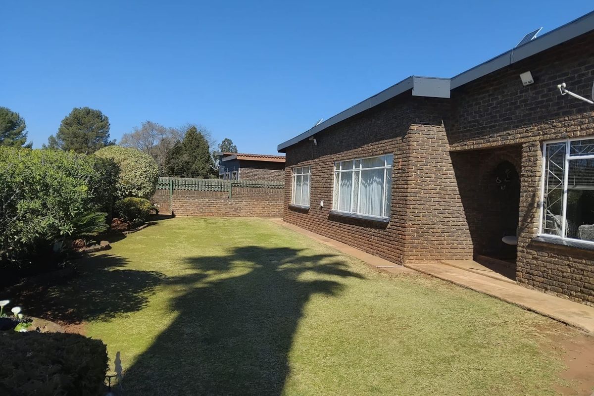 A well-maintained rear garden featuring a neat lawn, face brick exterior walls, and secure window treatments.
