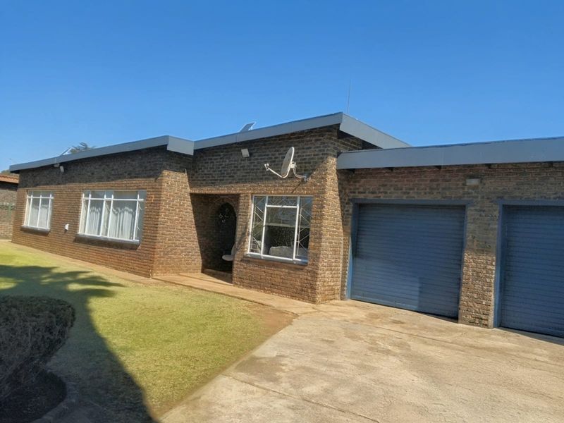 Front elevation of a single-story face brick house featuring a double garage, concrete driveway, and established lawn area.