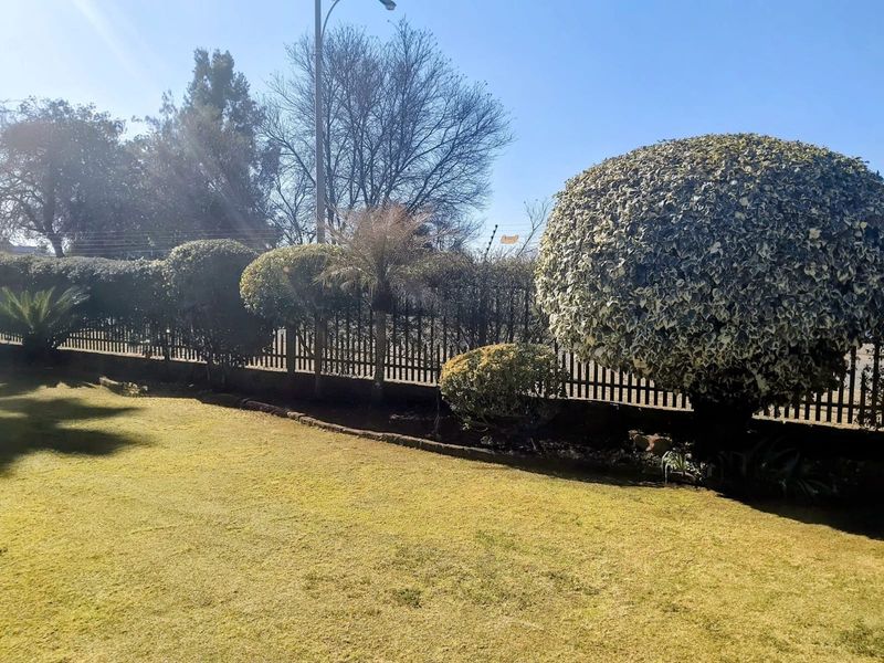 A well-maintained garden area featuring a manicured lawn, mature topiary shrubs, and secure metal perimeter fencing.