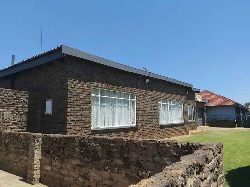 A single-story face brick house featuring metal window frames with security bars and a stone boundary wall in a residential setting.