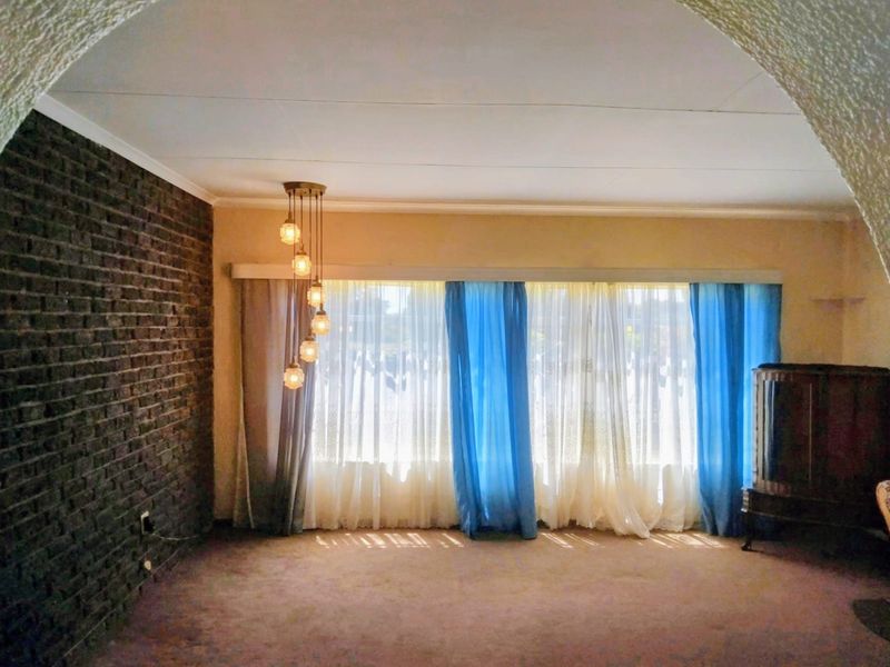 Spacious living room featuring an exposed brick feature wall, arched entryway, and large window with natural light.