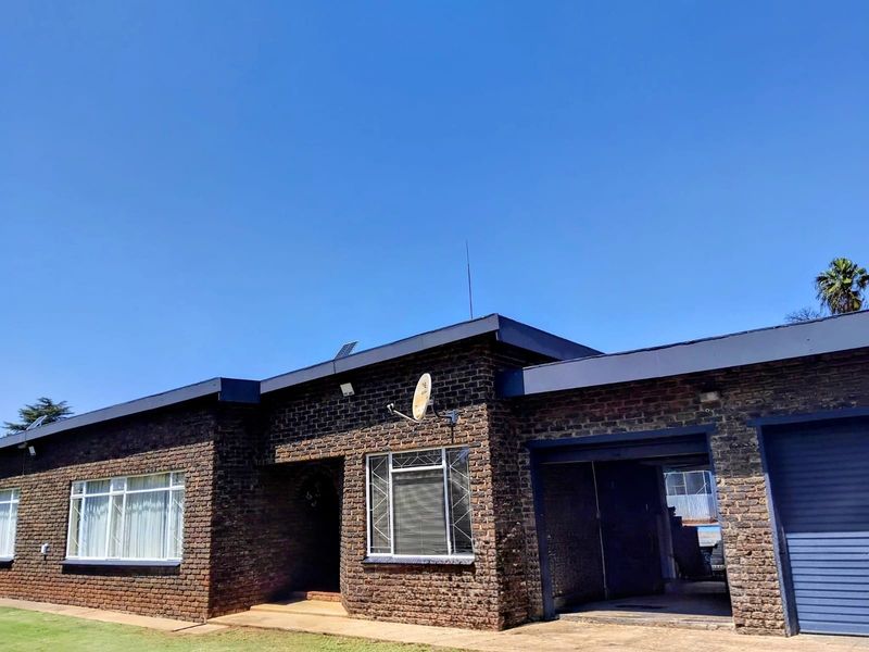 Front elevation of a single-story face brick house featuring a garage, aluminum window frames with security bars, and a clear blue sky background.