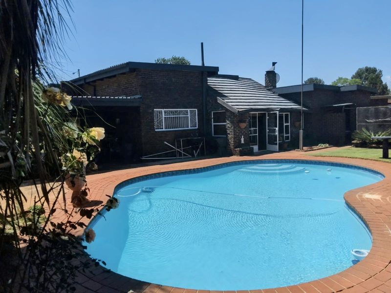 A backyard view featuring a swimming pool with brick paving, set against a face-brick house with a tiled roof.