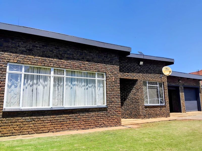 Front elevation of a face brick house featuring large windows with security bars, a flat roof, and an integrated garage.