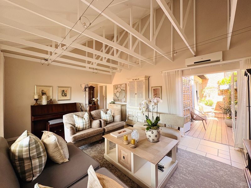 Spacious living room featuring high vaulted ceilings with exposed white timber trusses, tiled flooring, and direct access to an outdoor patio area.