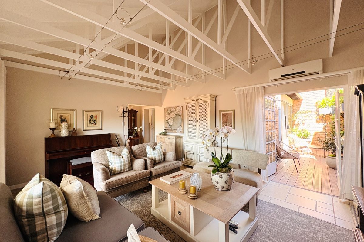 Spacious living room featuring high vaulted ceilings with exposed white timber trusses, tiled flooring, and direct access to an outdoor patio area.