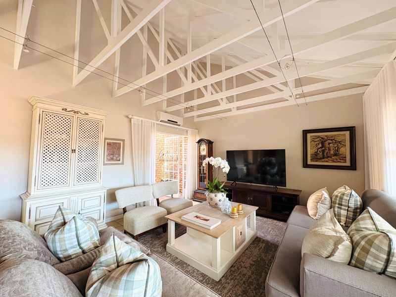 Spacious living room featuring high vaulted ceilings with exposed white timber trusses, neutral wall finishes, and direct access to an outdoor patio area.