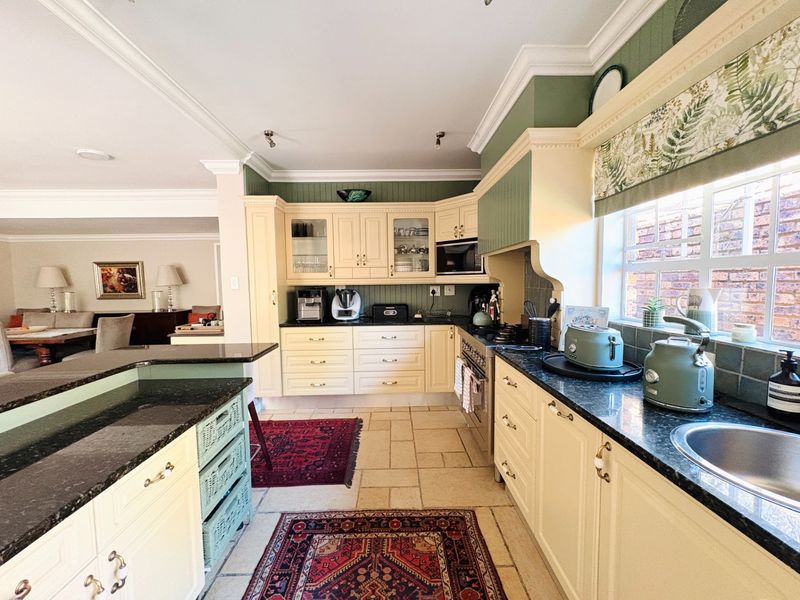 Open-plan kitchen featuring cream cabinetry, granite countertops, and integrated appliances, seamlessly flowing into the adjacent living area with tiled flooring throughout.