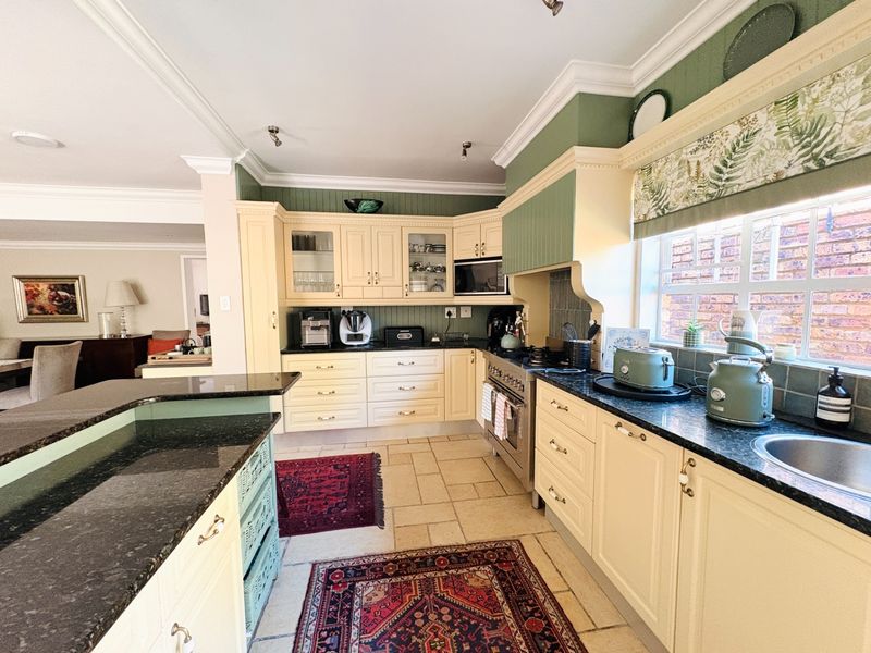 A well-maintained kitchen featuring cream cabinetry, dark granite countertops, a gas stove, and tiled flooring, seamlessly flowing into the adjacent living area.