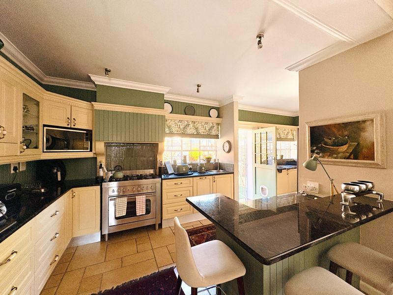 A charming country-style kitchen featuring cream cabinetry, dark granite countertops, a gas range, and a central island with breakfast bar seating.