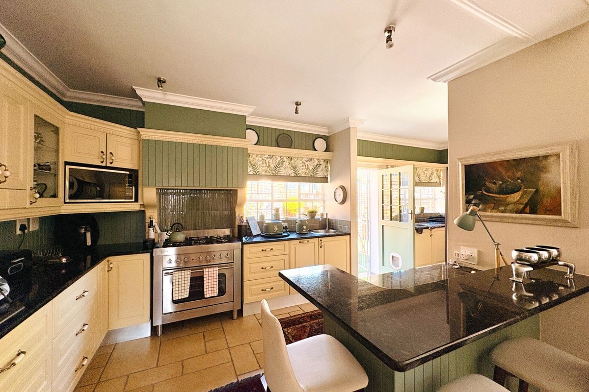 A charming country-style kitchen featuring cream cabinetry, dark granite countertops, a gas range, and a central island with breakfast bar seating.