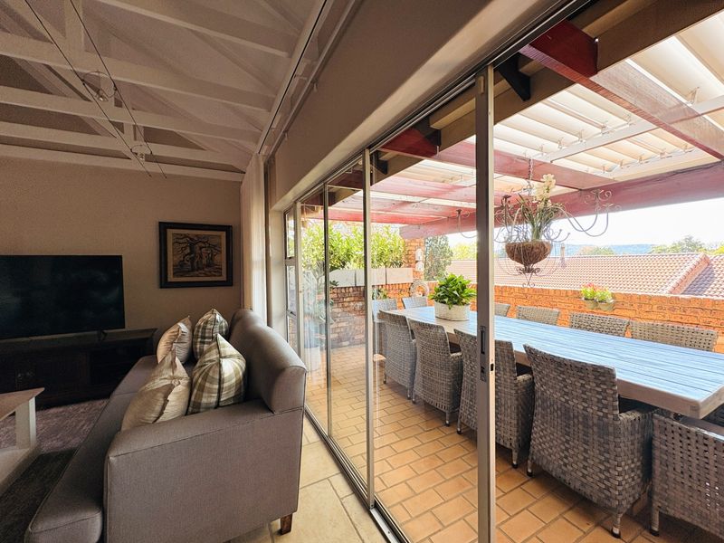 Open plan living area seamlessly connecting to a covered outdoor patio through large sliding glass doors, featuring exposed beam ceilings and brick accents.