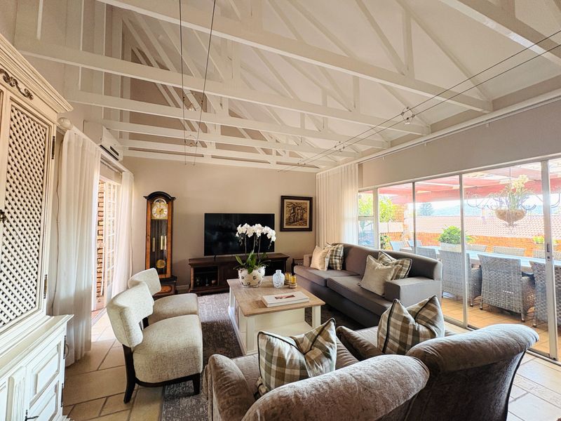 Spacious living room featuring a high vaulted ceiling with exposed white timber trusses, tiled flooring, and large sliding glass doors leading to an outdoor patio.