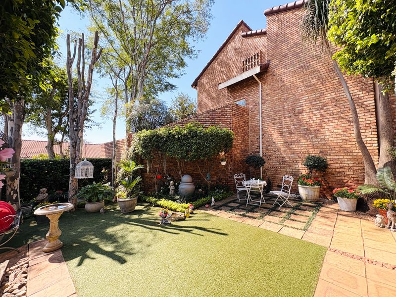 A private rear garden featuring a brick townhouse facade, artificial lawn, paved patio area, and established landscaping.