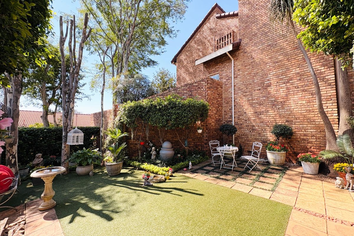 A private rear garden featuring a brick townhouse facade, artificial lawn, paved patio area, and established landscaping.