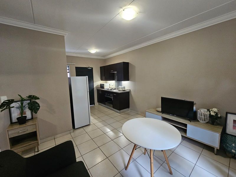 Open-plan living area featuring a compact kitchen with dark cabinetry, built-in oven, hob, and tiled flooring throughout the space.