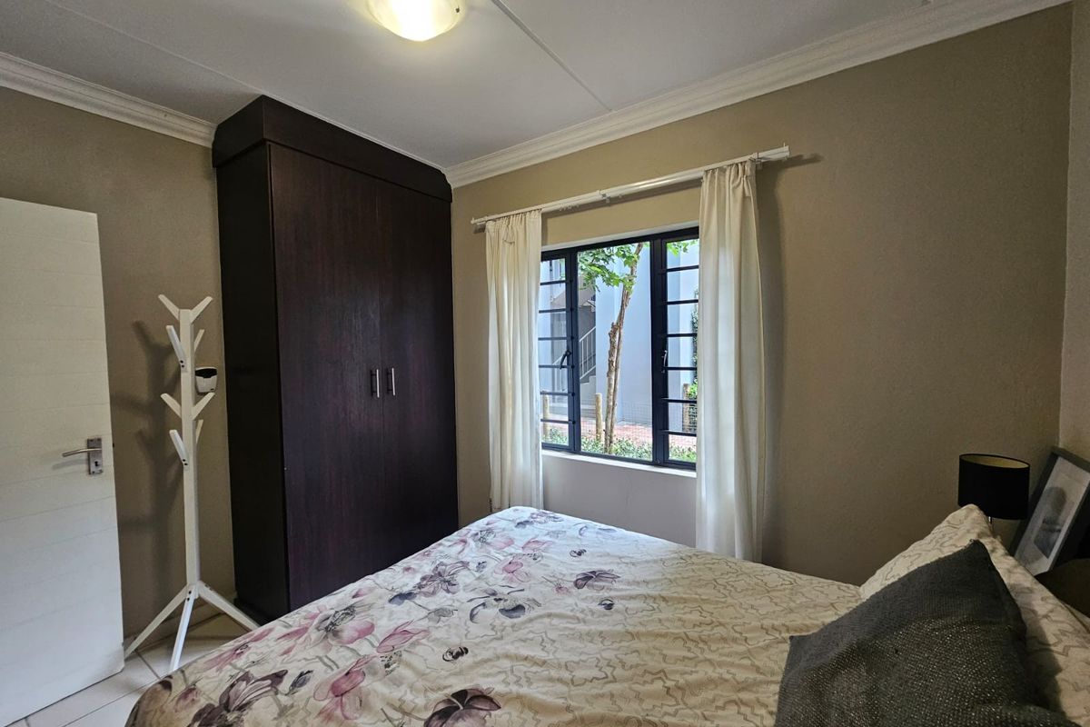 A bedroom featuring tiled flooring, a built-in dark wood wardrobe, and a window with security bars overlooking the exterior.