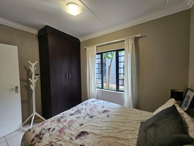 A bedroom featuring tiled flooring, a built-in dark wood wardrobe, and a window with security bars overlooking the exterior.