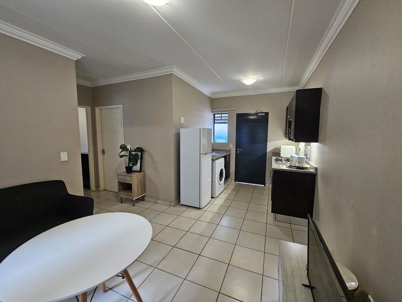 Open-plan living area featuring tiled floors, a compact kitchen with dark cabinetry, granite countertops, and integrated laundry plumbing.